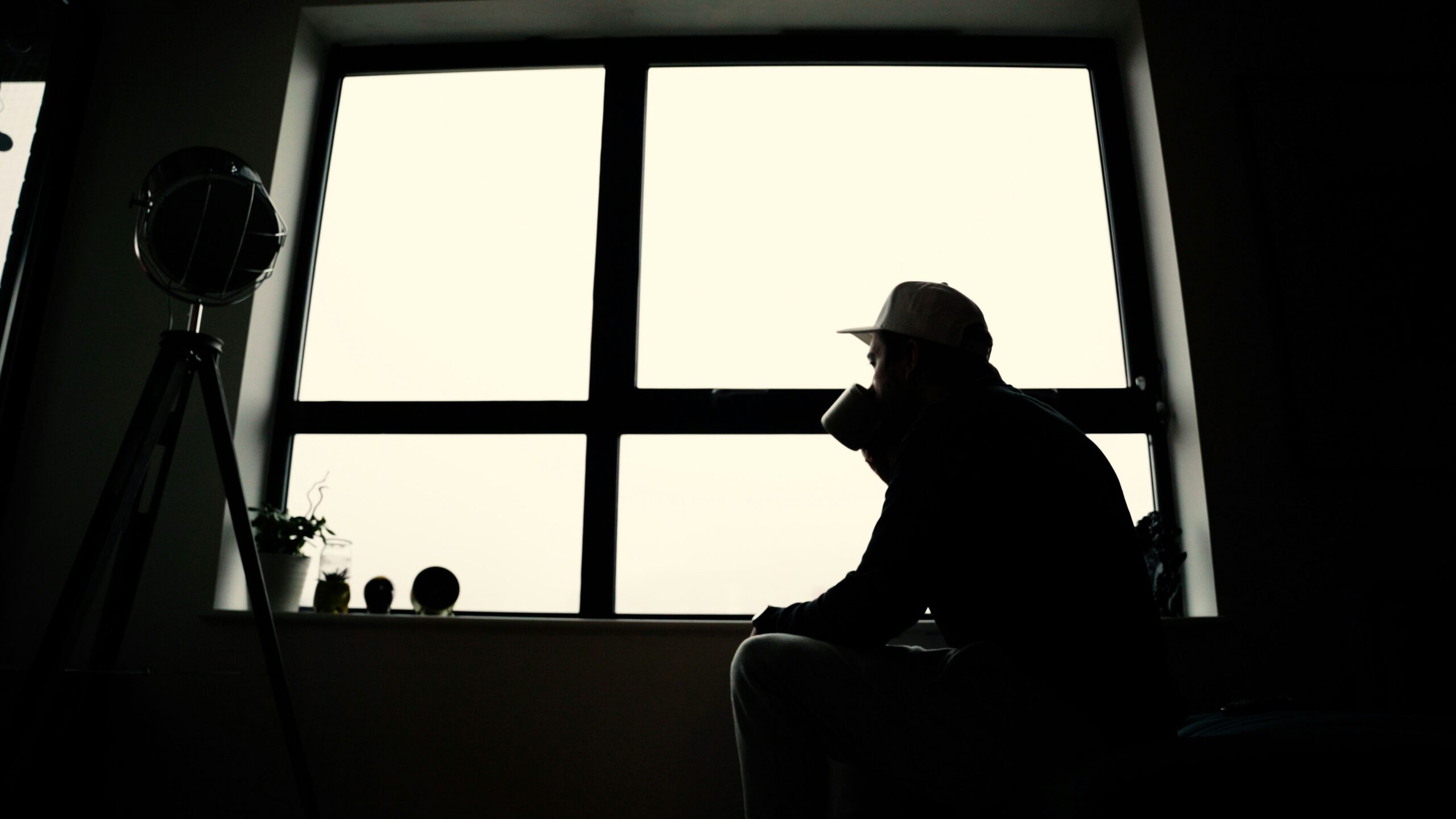 Man alleen bij raam in gedachten verzonken als symbool voor zelfsabotage en innerlijke strijd